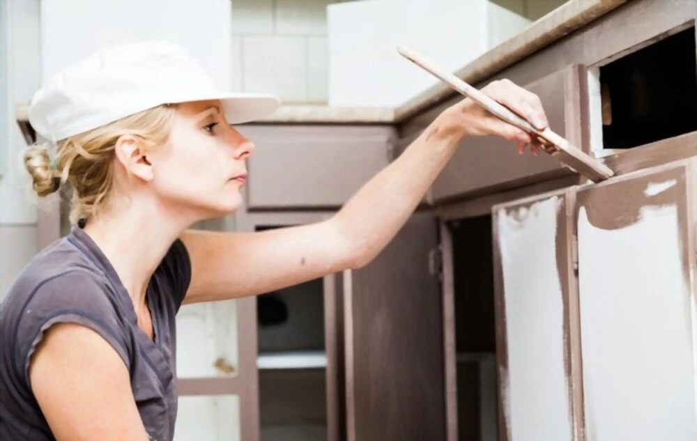 closeup woman holding paint brush painting kitchen cabinets