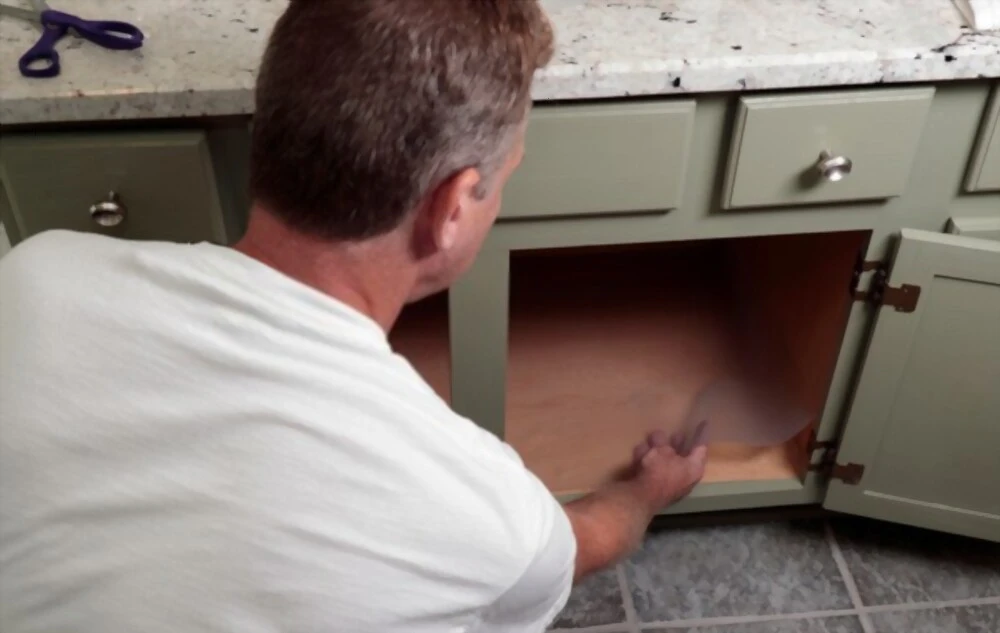 a man lines the bottom of a cabinet with a plastic sheet